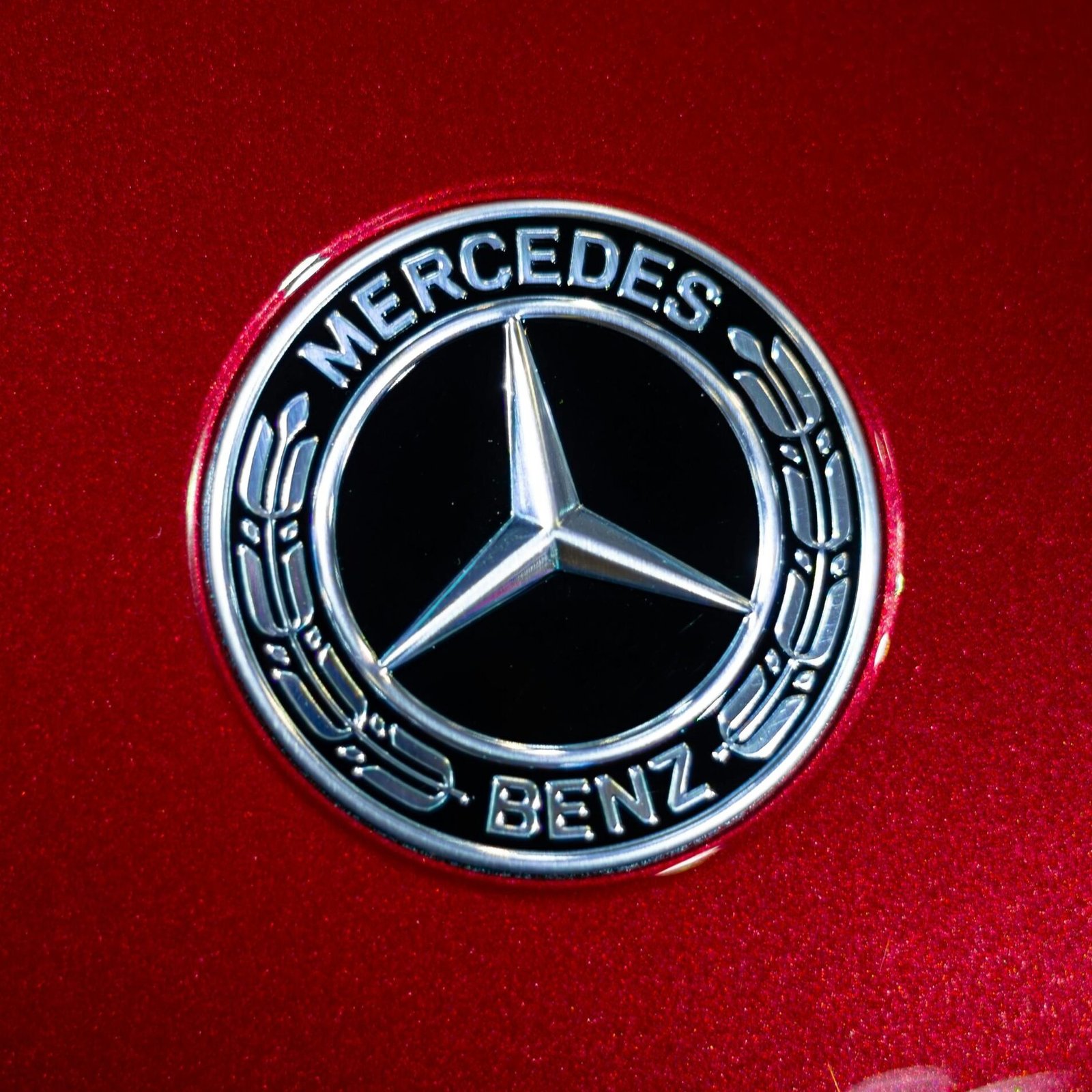 Detailed view of the Mercedes-Benz emblem on a sleek red car surface.